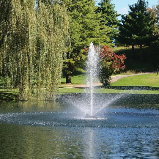 Fountain in a pond with trees and grass in the background